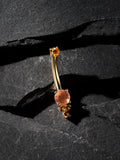 Gold belly button ring with orange gemstones on a dark stone surface