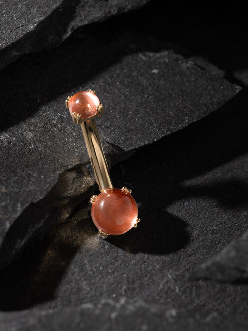 Gold barbell with peach-colored beads on a dark stone surface