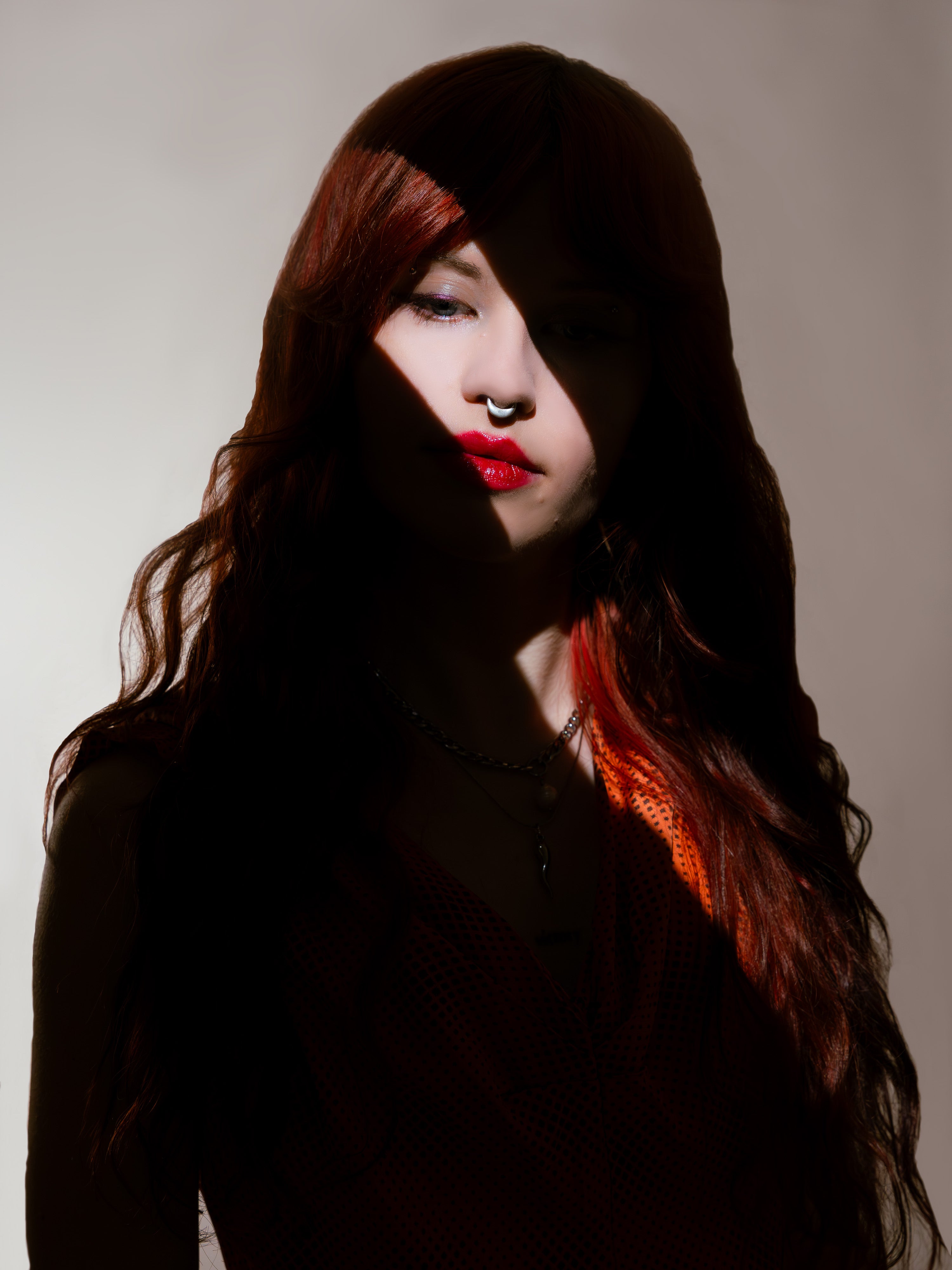 woman with long red hair and red lipstick wearing a septum piercing against a neutral background